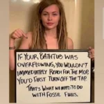 A picture of an attractive young woman with long blonde dreads standing in a shower/bath stall without any clothing.  A sign she is standing behind is blocking the view of her torso.  "If your bathtub was overflowing you wouldn't immediately reach for the mop. You would first turn off the tap. That is what we need to do with fossil fuels."